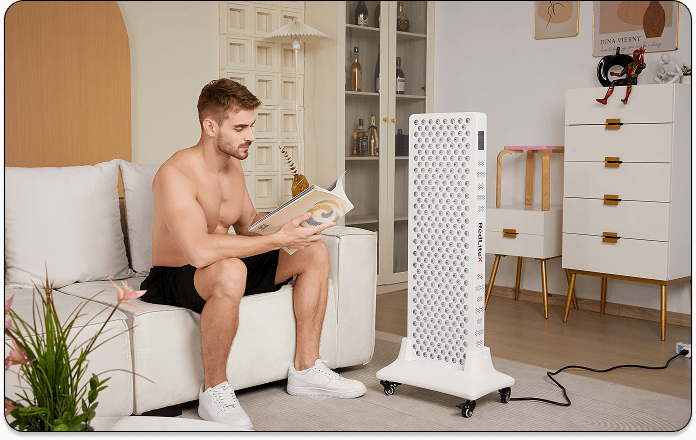 A model sitting next to a red light therapy device while reading a book